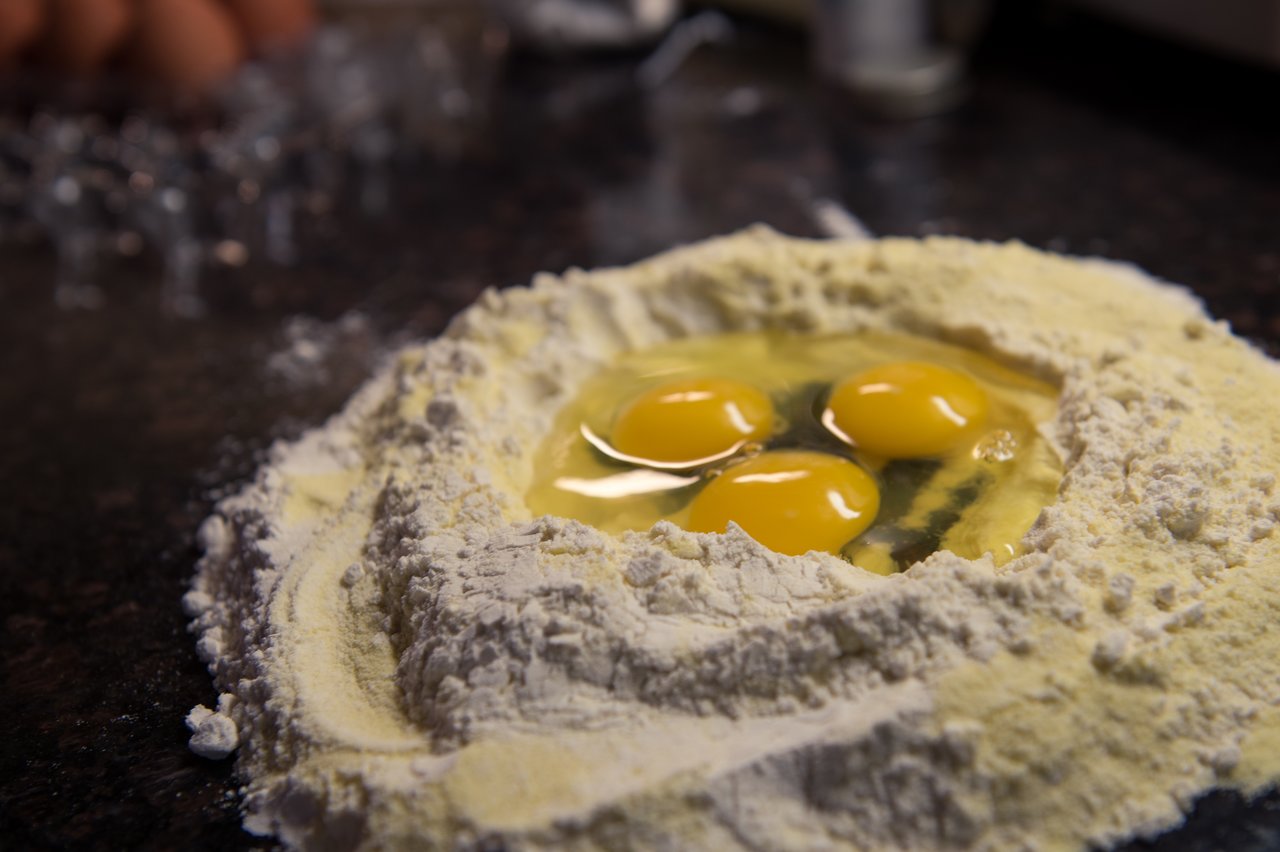 A mound of flour with three cracked eggs in the center, ready for making homemade pasta dough.