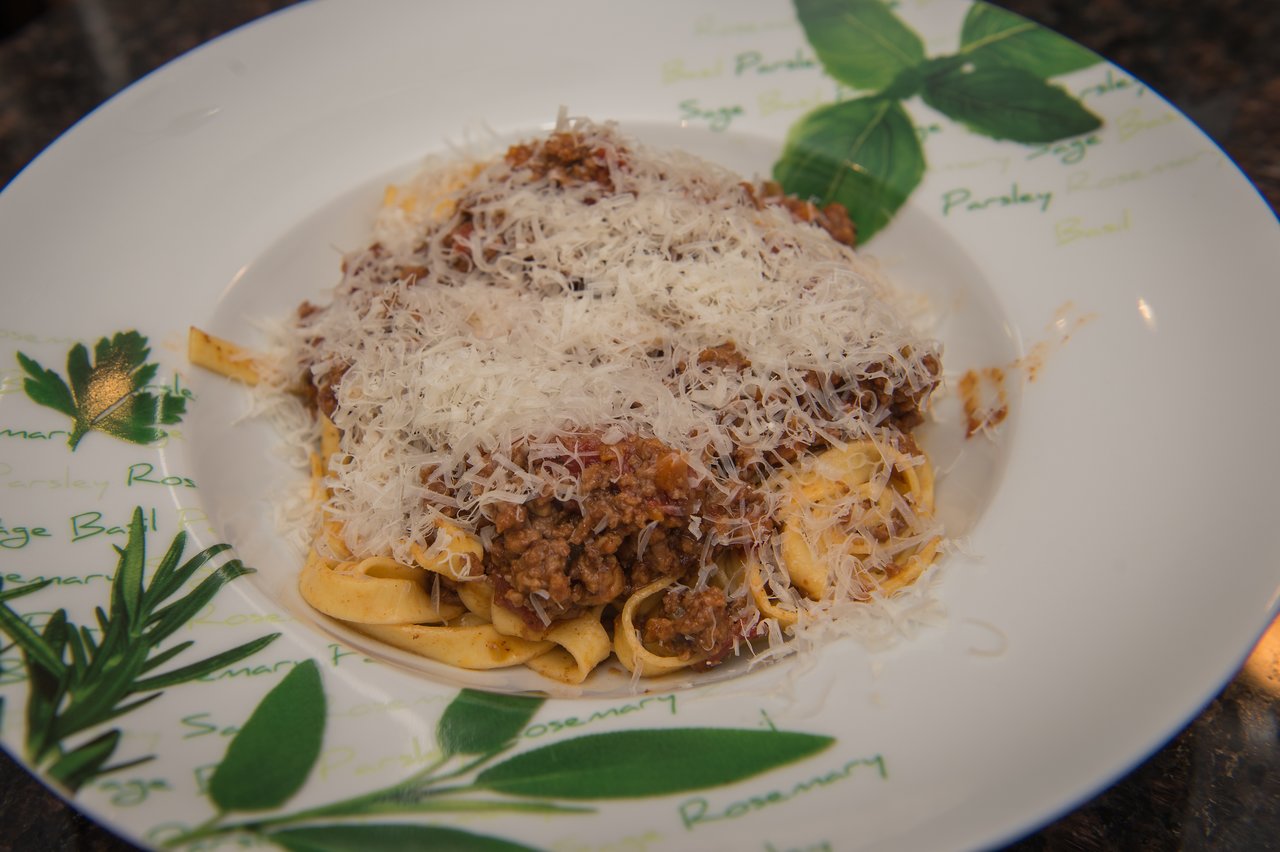 A plate of pasta with meat sauce, topped with grated cheese, served on a decorative dish.