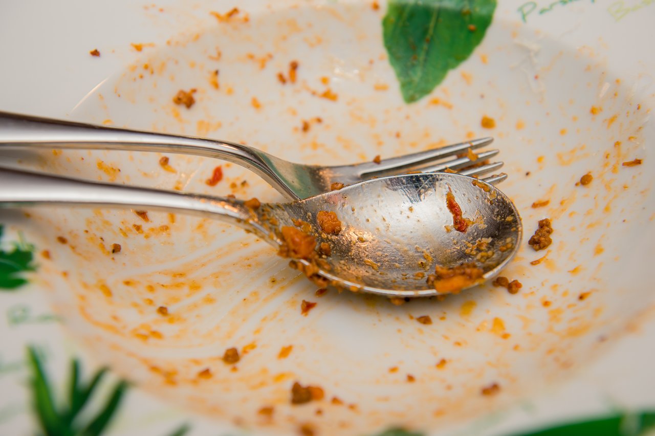 An empty plate with pasta sauce remnants, a spoon, and a fork resting on it.
