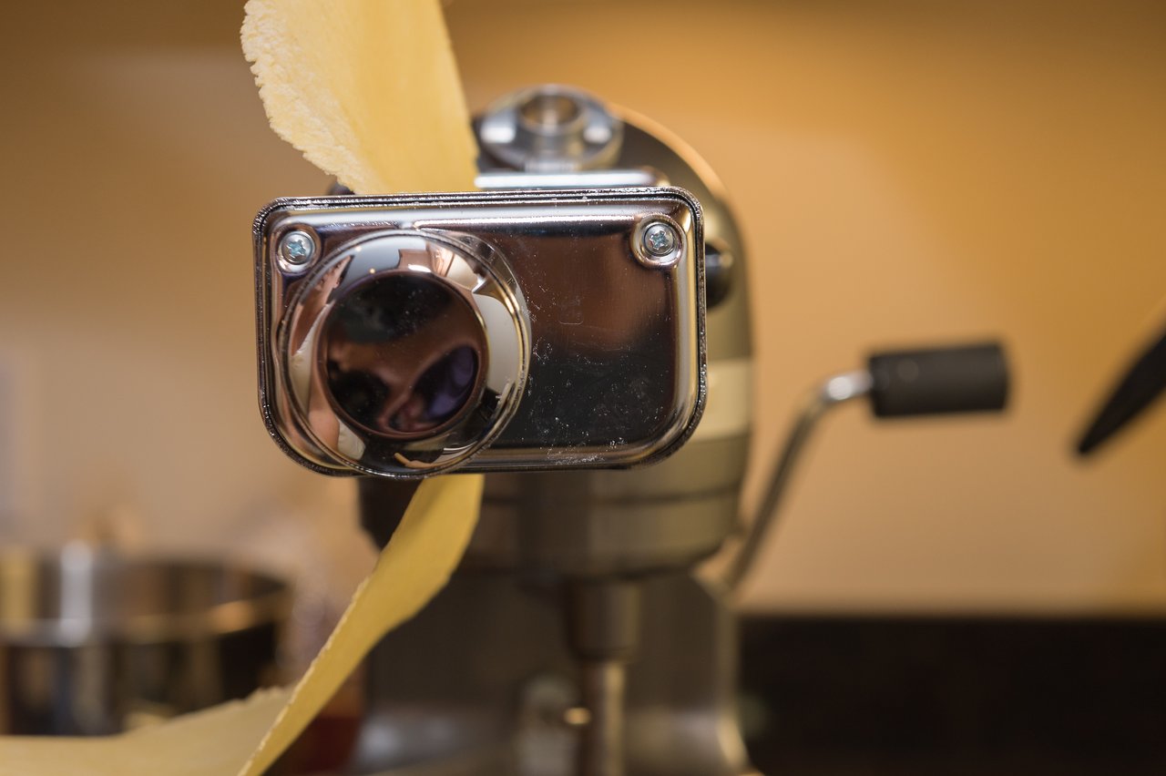 A pasta machine rolls out a sheet of fresh dough in a kitchen.