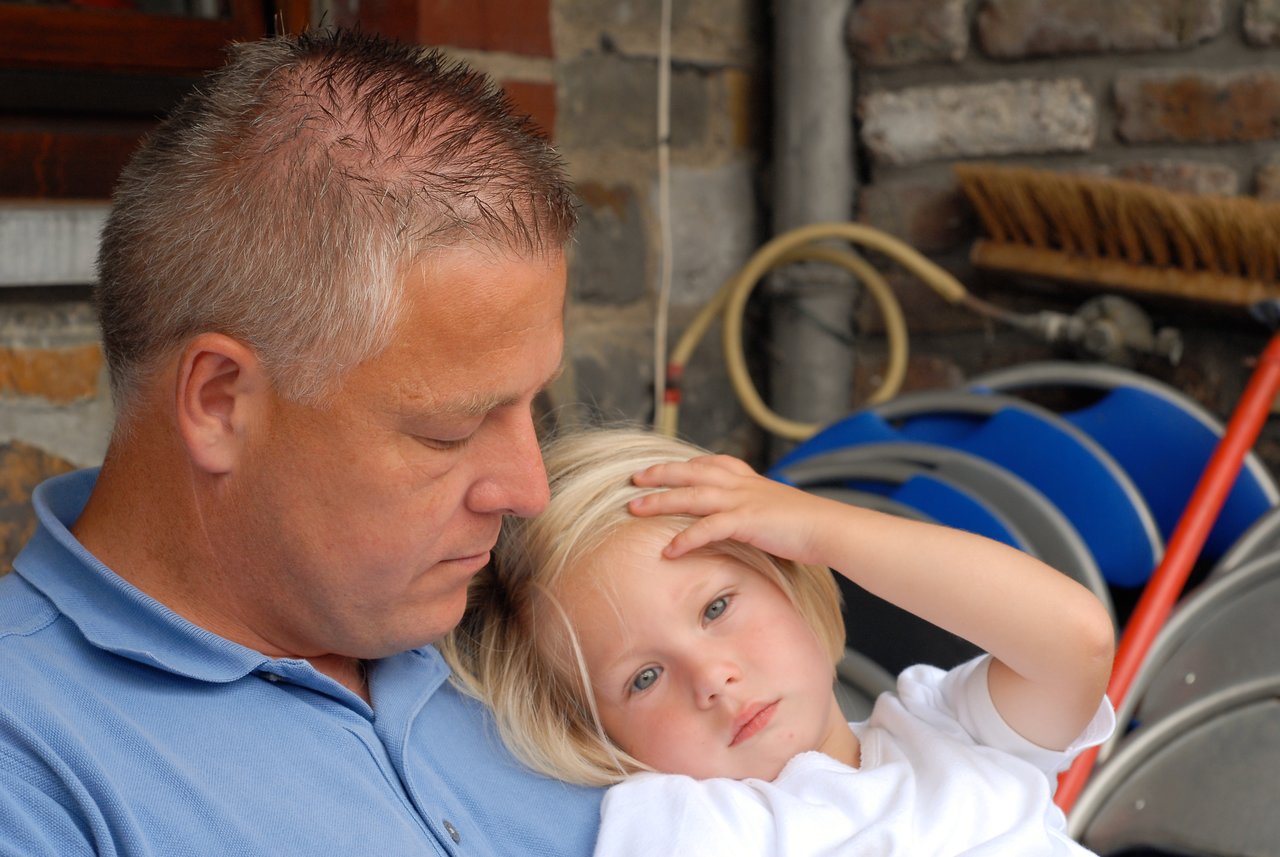A man in a blue shirt holds a young child in his arms.