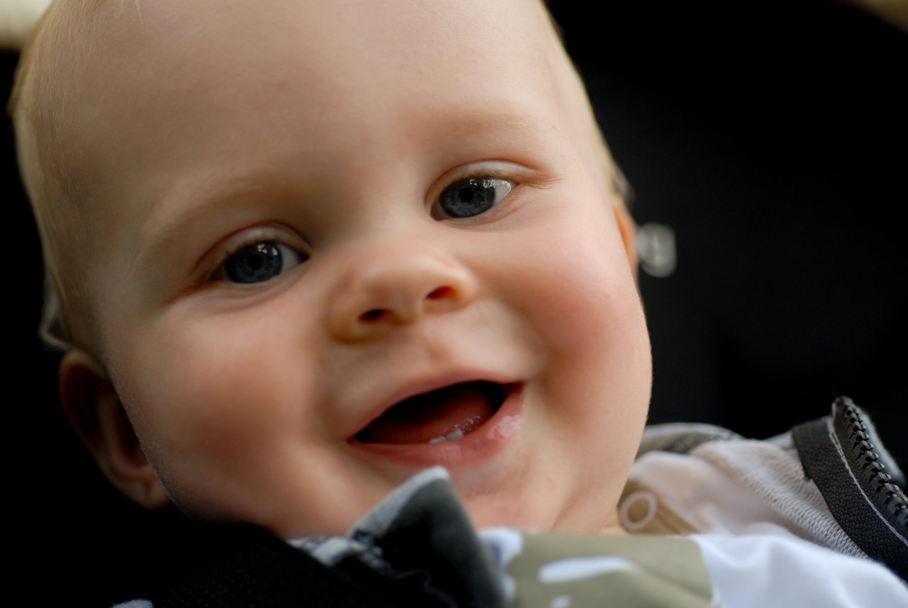 A close-up of a smiling baby with bright eyes and a joyful expression, looking directly at the camera.