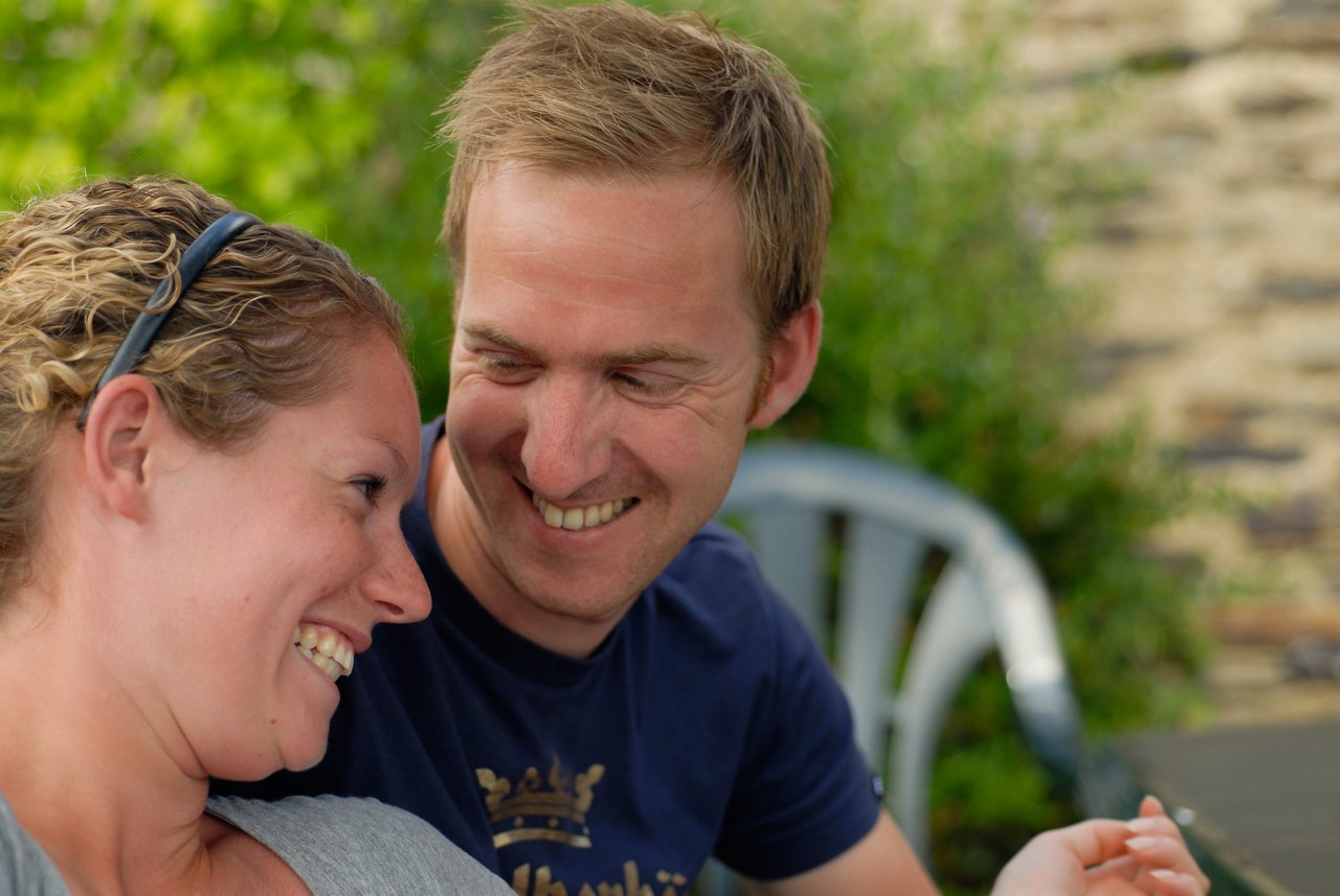 A man and woman sit closely together, smiling and laughing while looking at each other.