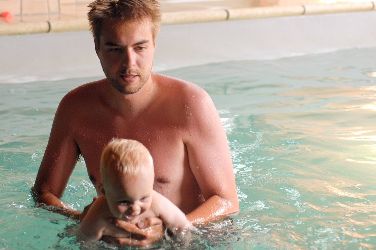 A man holds a smiling baby in a swimming pool, keeping them steady in the water.