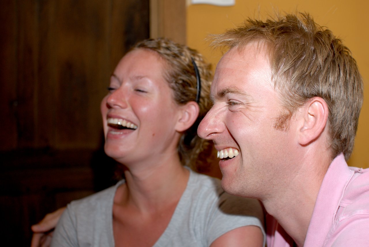 Two people laughing together in a close-up shot, appearing to enjoy a joyful moment indoors.