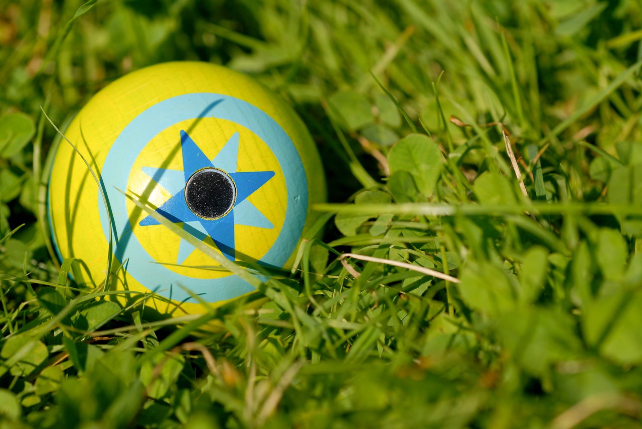 A colorful wooden ball with a blue star design lies on the grass.