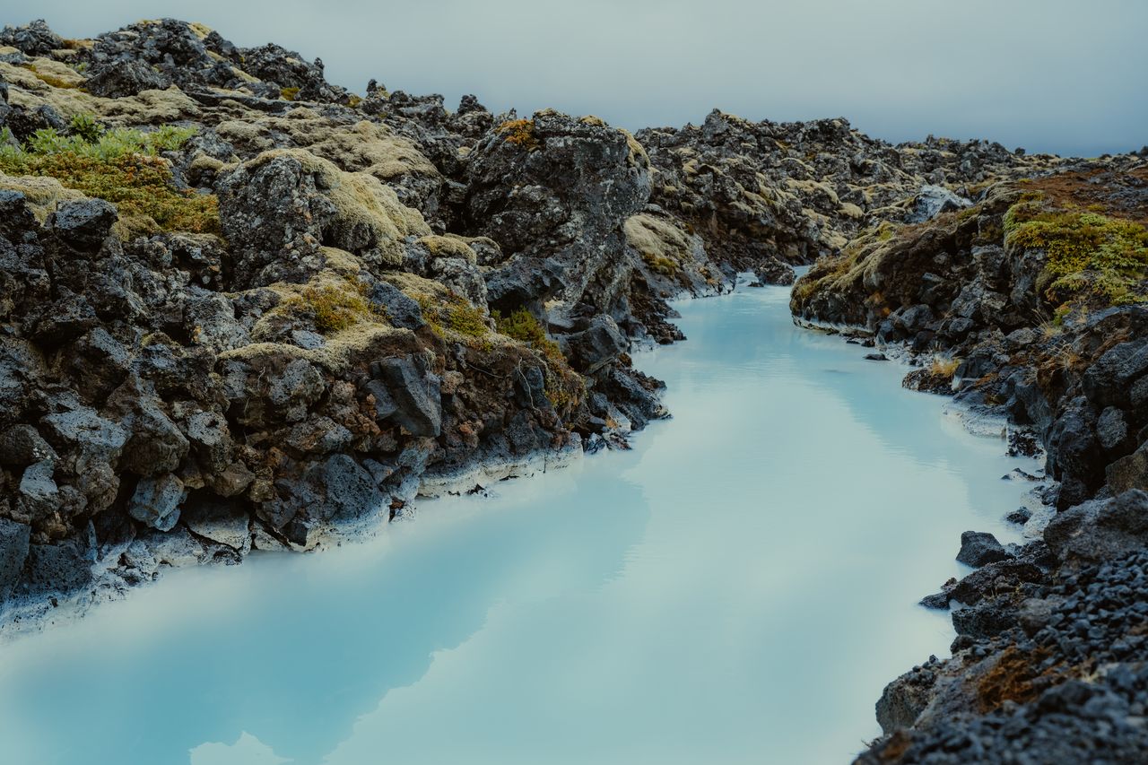 A milky blue geothermal pool surrounded by dark volcanic rocks and moss in Iceland's Blue Lagoon.