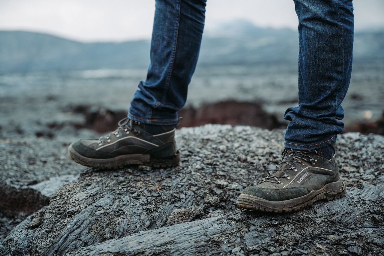 Close-up of a person wearing hiking boots and jeans, standing on hardened lava rock near Gerlingadalur volcano in Iceland.
