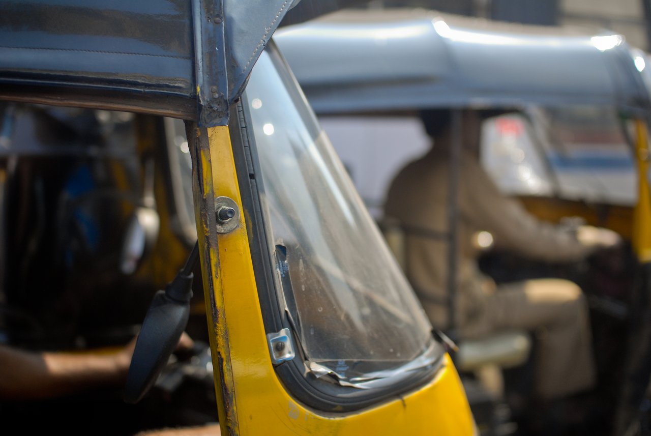Close-up of a yellow auto rickshaw with a driver in uniform operating another rickshaw in the background.