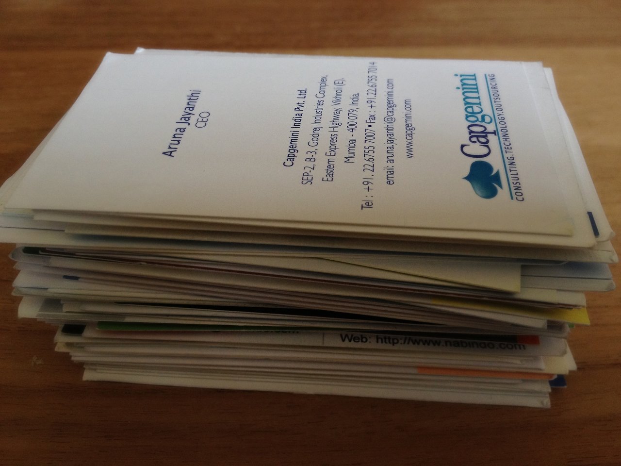 A stack of business cards placed on a wooden surface, with one card from Capgemini visible on top.