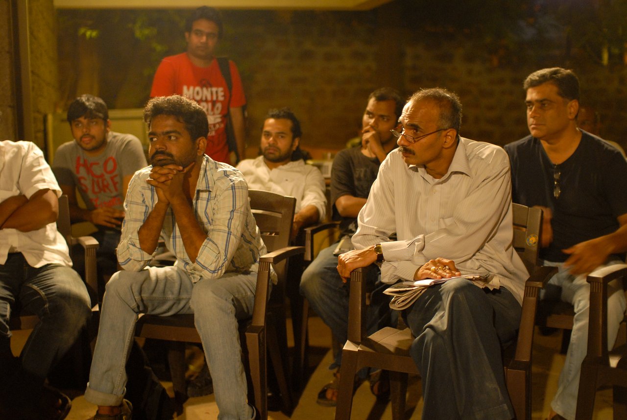 A group of people sit closely together, attentively listening and engaged in a discussion during an evening gathering.
