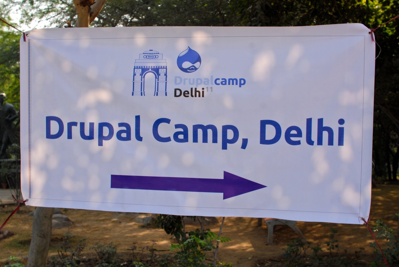 A banner for Drupal Camp Delhi with a directional arrow pointing right.