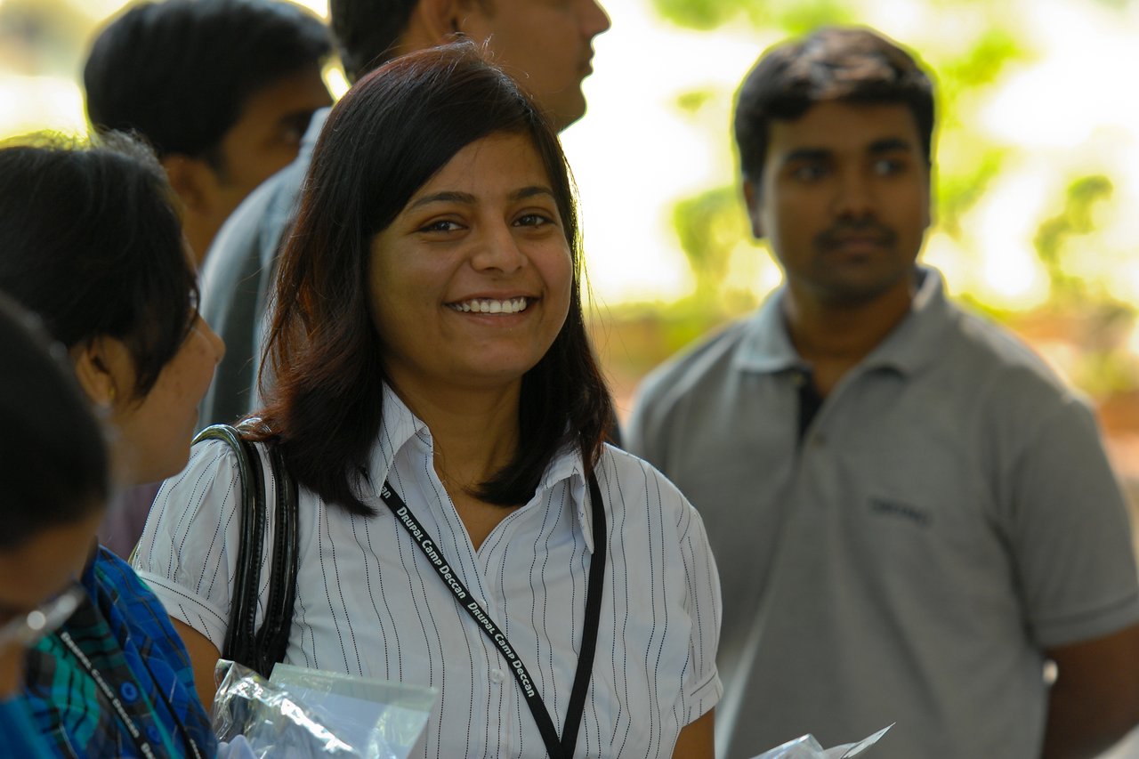 A smiling woman wearing a lanyard stands among a group of people at a Drupal event.