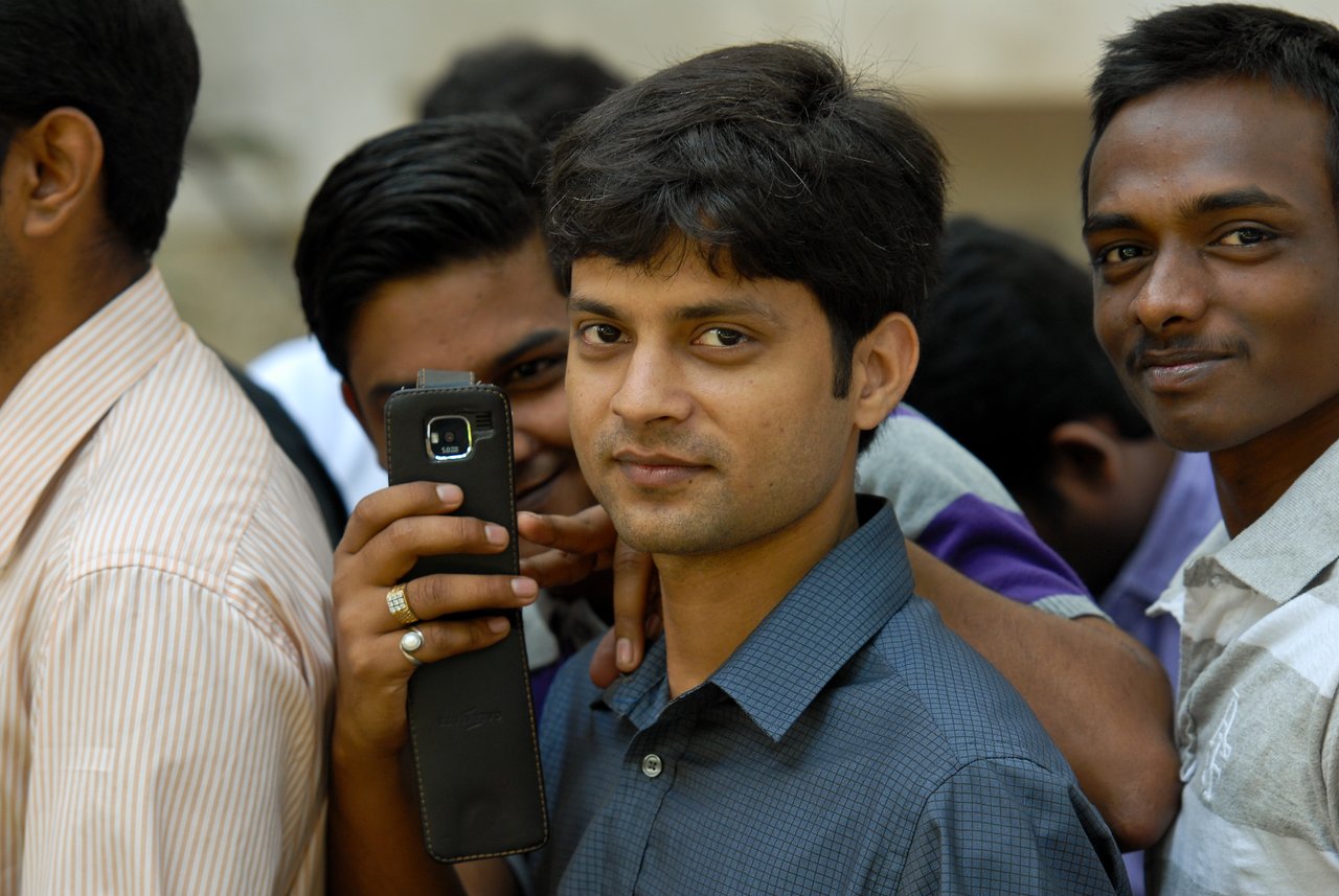 A group of men standing close together, one holding a phone and another looking directly at the camera.