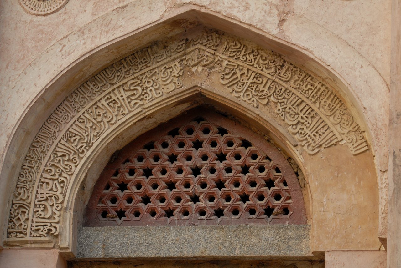 An arched entrance to an Indian tomb with intricate carvings and geometric latticework above the doorway.