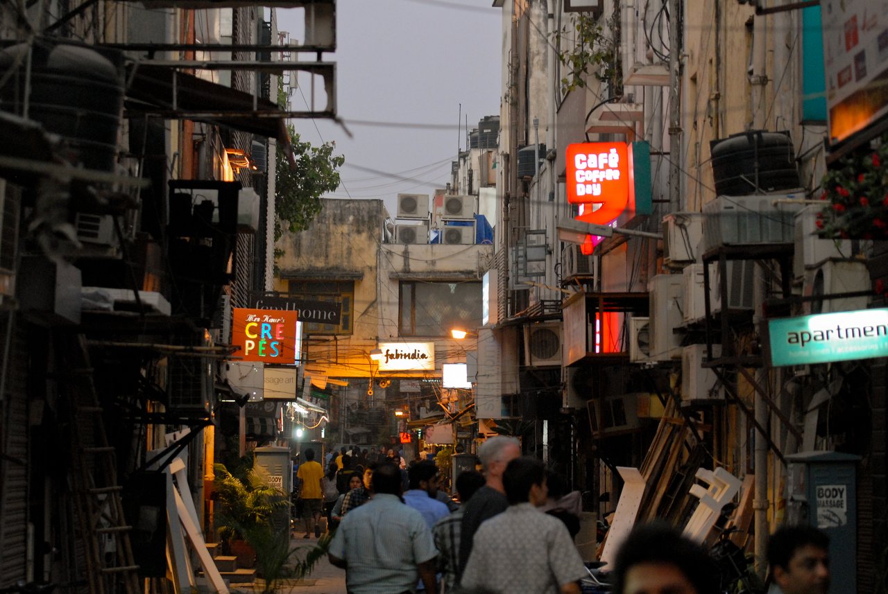 People walk through a narrow street lined with shops and glowing signs during an evening shopping trip.