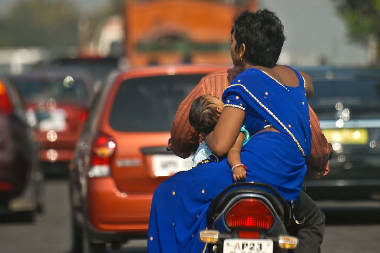 A man rides a motorcycle with a woman and a baby sitting behind him in busy traffic.