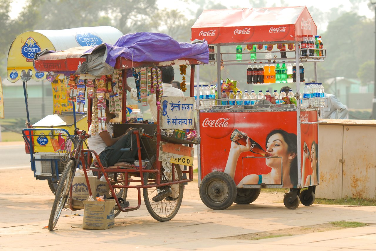 Street vendors sell snacks and drinks from colorful carts, with bottled beverages and packaged goods displayed for customers.
