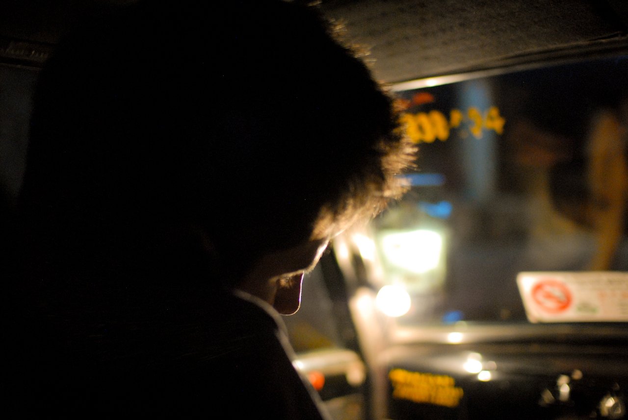A person is working inside a car at night, illuminated by a small light near the dashboard.