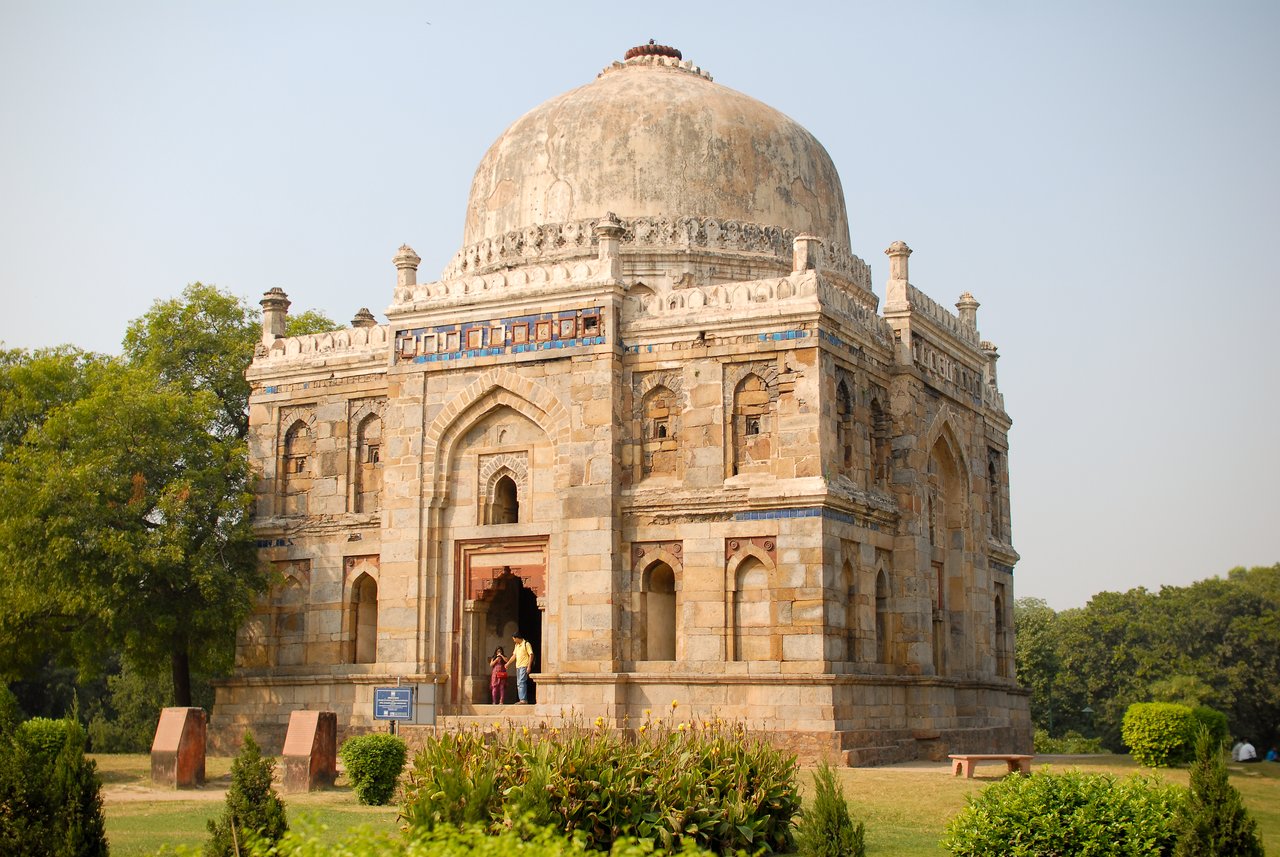 A historic stone tomb with a large dome in Lodhi Gardens, New Delhi, with people entering the doorway.