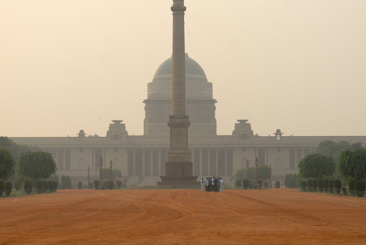 A group of people stands near a tall monument in front of the Presidential Palace in New Delhi, India.