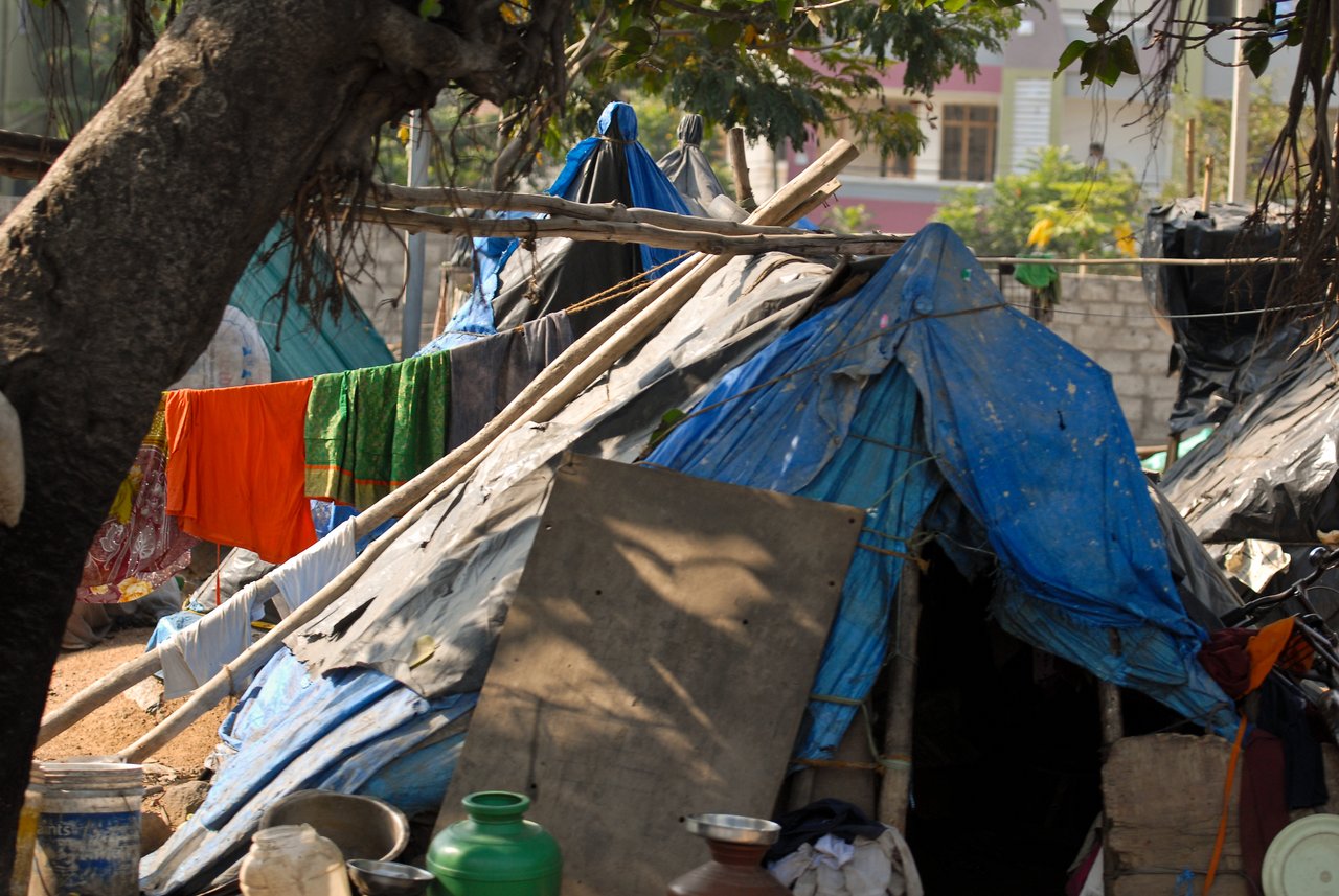 Makeshift shelters with blue tarps and wooden supports, with clothes hanging to dry on a line nearby.