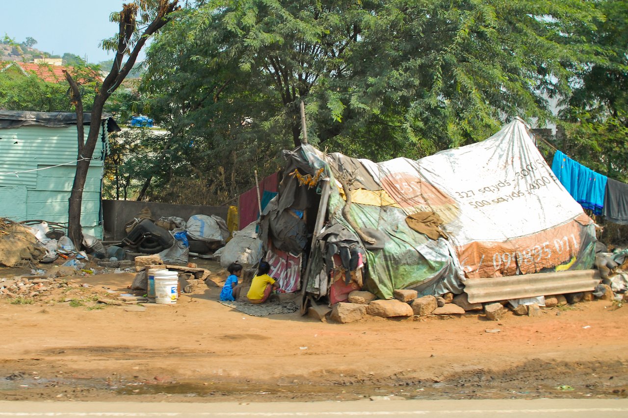 A makeshift shelter made of tarps and cloth, with two children sitting outside on the ground.