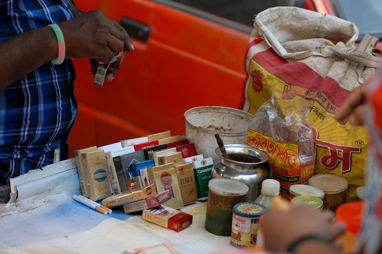 A street vendor arranges cigarette packs and tobacco products on a small table while a customer reaches to buy.
