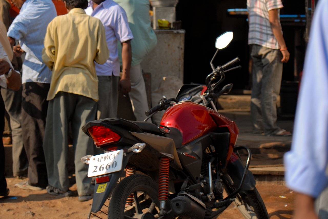 A red motorcycle is parked in the foreground while a group of people stand and talk on the street.