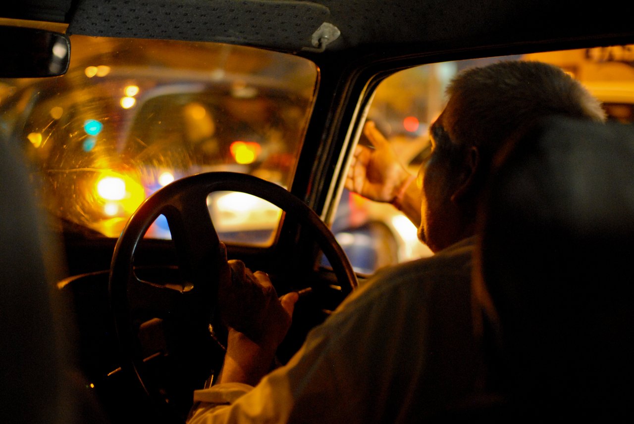 A driver grips the steering wheel and gestures angrily outside the car window in nighttime traffic.