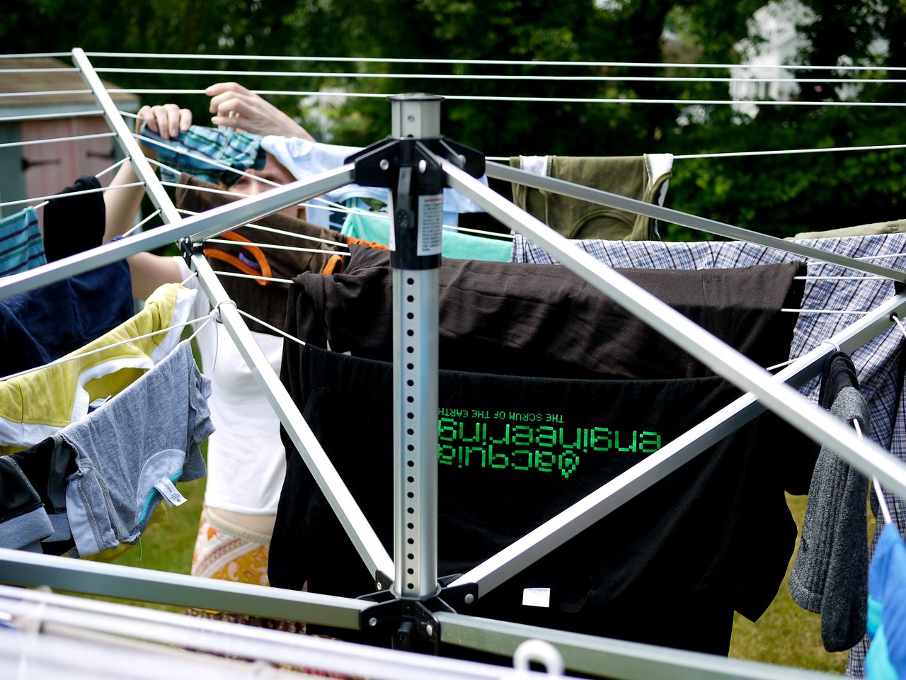 A person hangs laundry on a rotary clothesline, with various garments drying in the sunlight.
