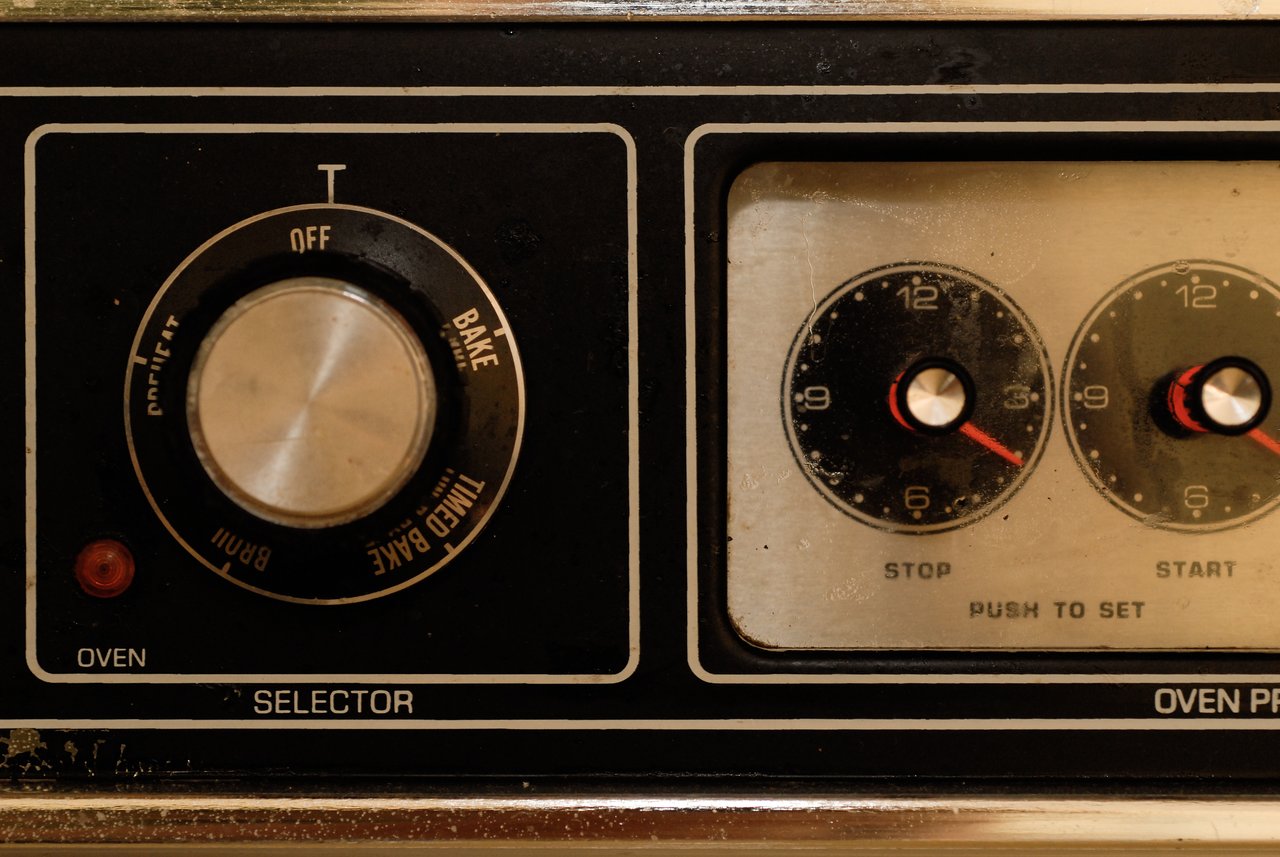 Close-up of an oven control panel with a selector knob and two dials for setting the timer.