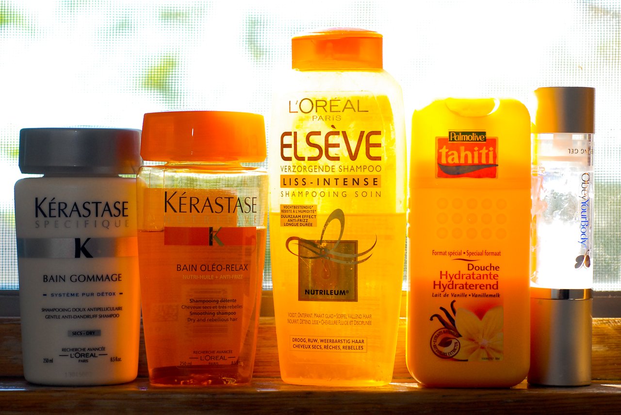 Five bottles of shower gel and shampoo are lined up on a windowsill, illuminated by sunlight.