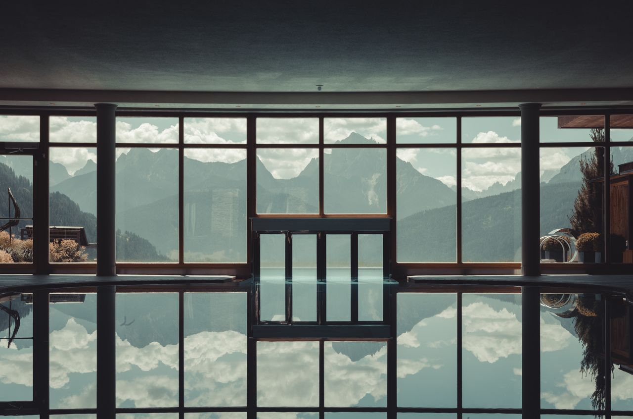 An indoor-outdoor pool at Hotel Alpen Tesitin with large windows showing a mountain view.