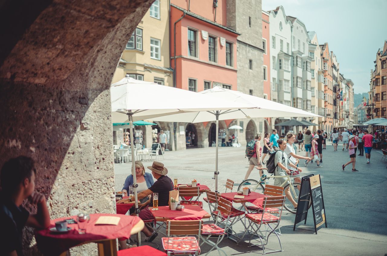 Outdoor café with red tablecloths in Innsbruck's old town, with people dining and pedestrians walking nearby.
