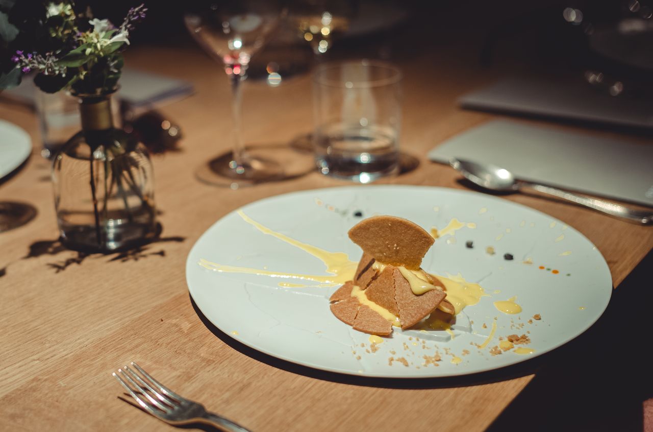 A deconstructed lemon tart with broken pastry and yellow cream is arranged on a plate, resembling a dropped dessert.