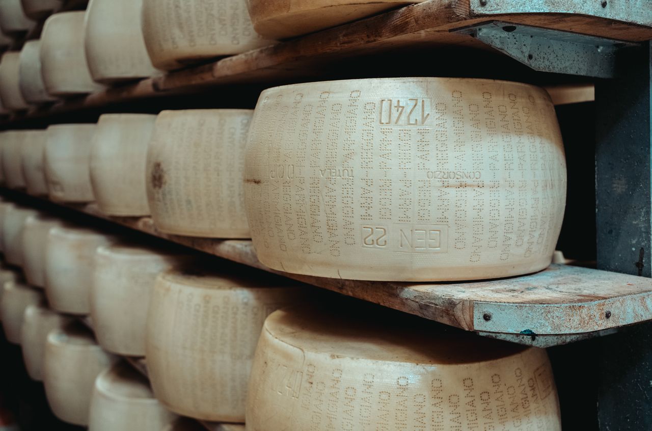 Stacks of large Parmigiano Reggiano cheese wheels aging on wooden shelves in a storage room.