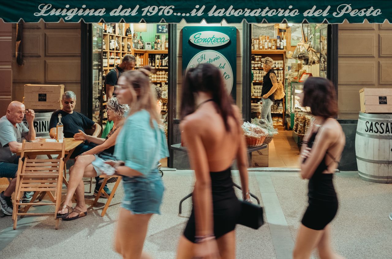 People sitting at an outdoor café table watch as blurred pedestrians walk past on a busy street in Levanto.