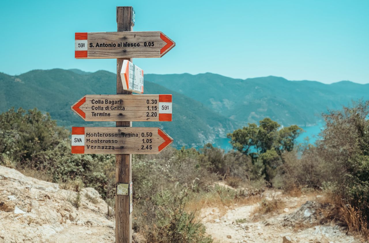 Wooden trail signs with red and white markings point to different hiking routes along the SVA path in Cinque Terre.