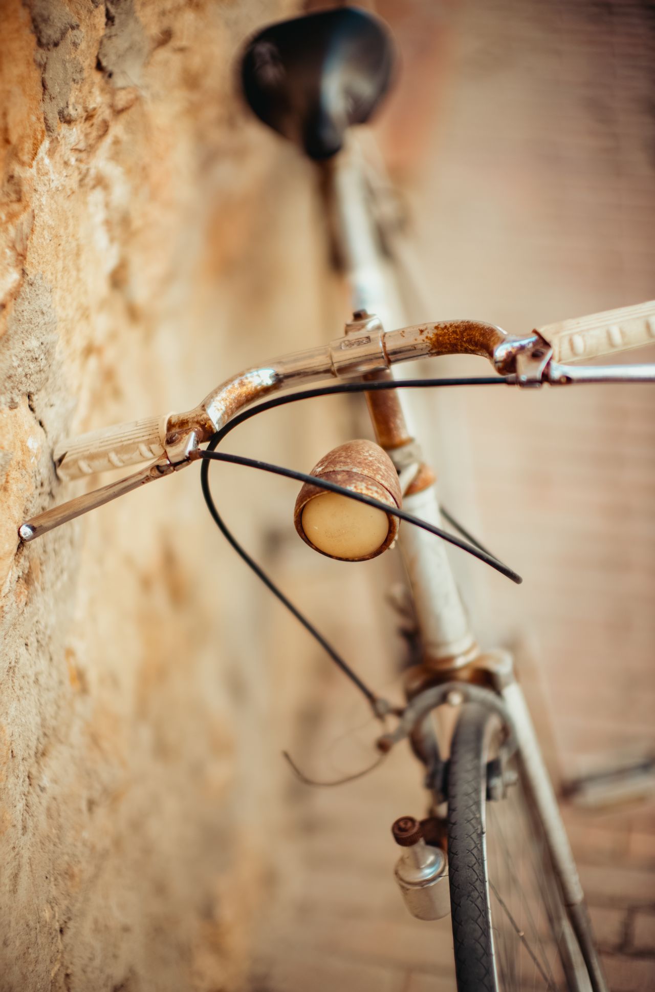 A rusty old bicycle leans against a textured stone wall in Pienza, Italy.