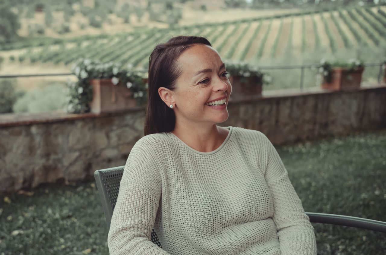 A woman sits outdoors, smiling and enjoying a relaxed moment at Dievole.