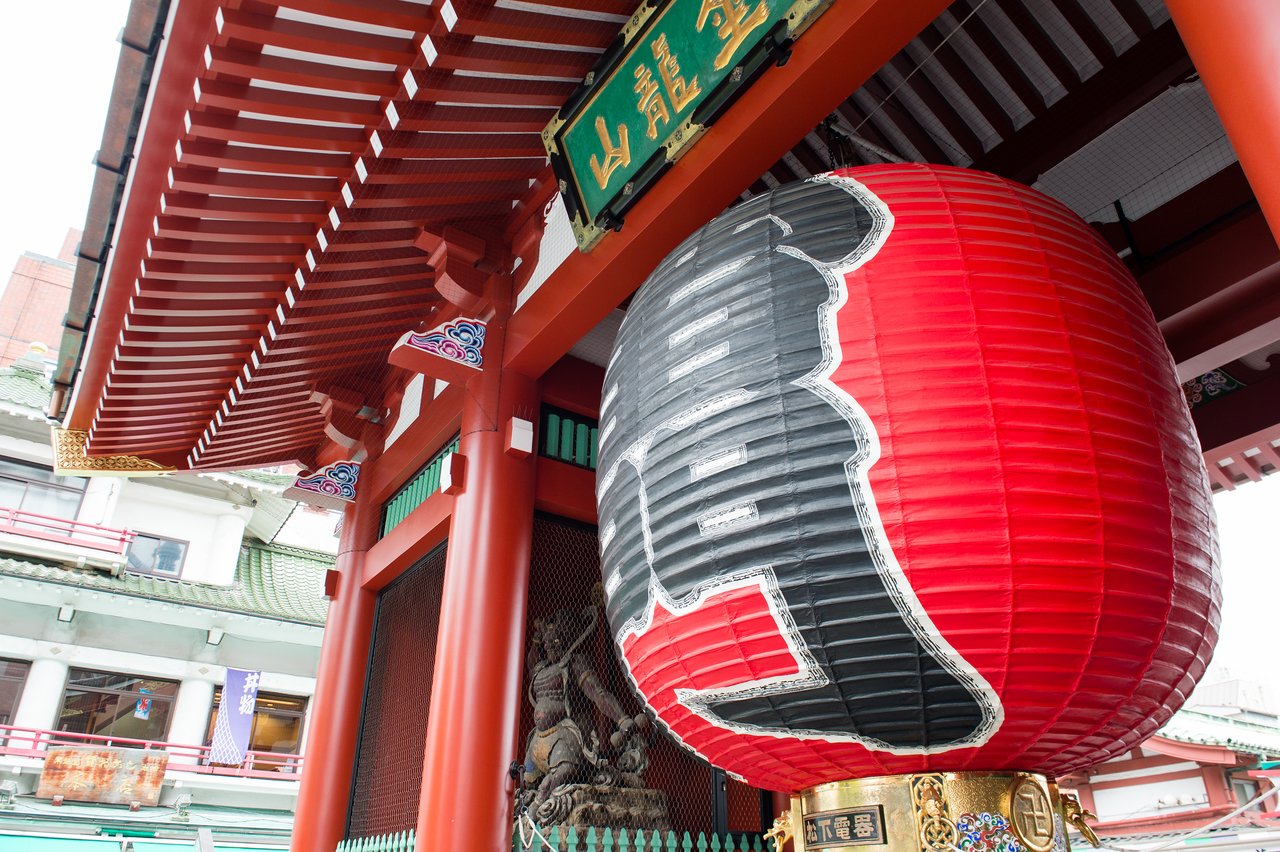 A large red and black paper lantern hangs at the entrance of a traditional Japanese temple.