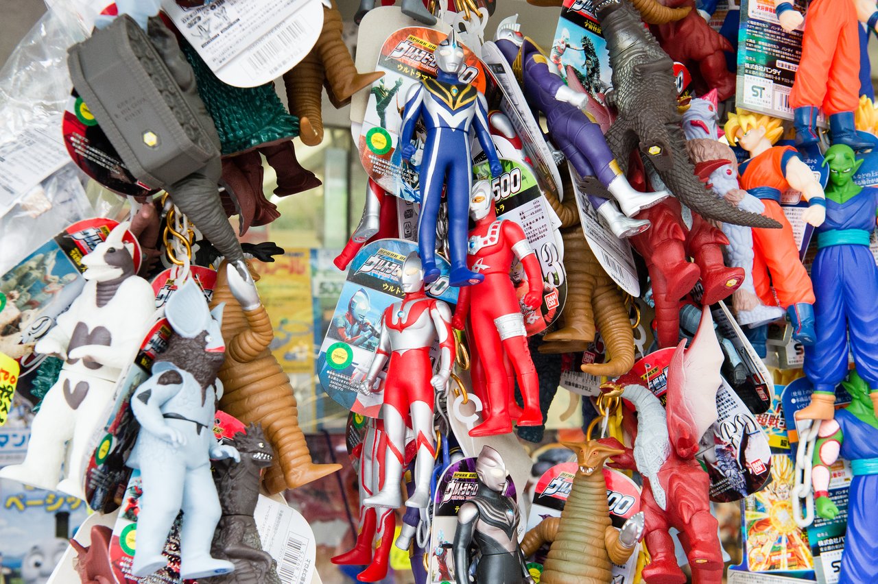 A display of colorful Japanese action figures, including Ultraman, Dragon Ball characters, and various monsters, hanging in a shop.