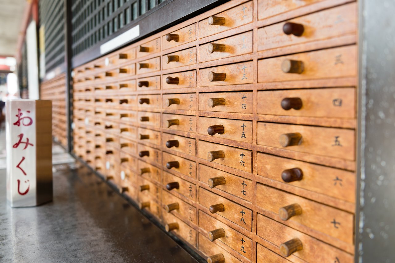 A wooden omikuji fortune drawer set with numbered compartments and a metal container for drawing fortune sticks.