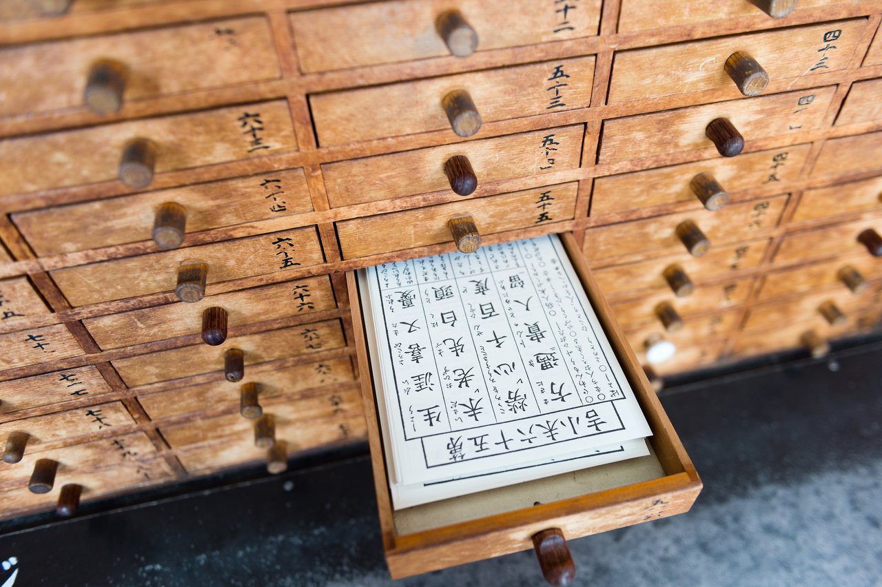 A wooden drawer with Japanese characters is open, revealing a printed paper with more Japanese text inside.