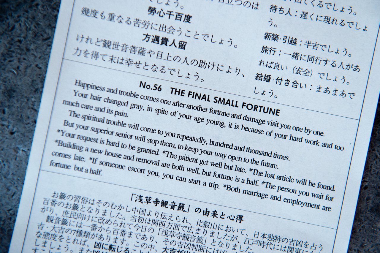 A close-up of a Japanese fortune slip with English and Japanese text, predicting mixed fortunes and future challenges.
