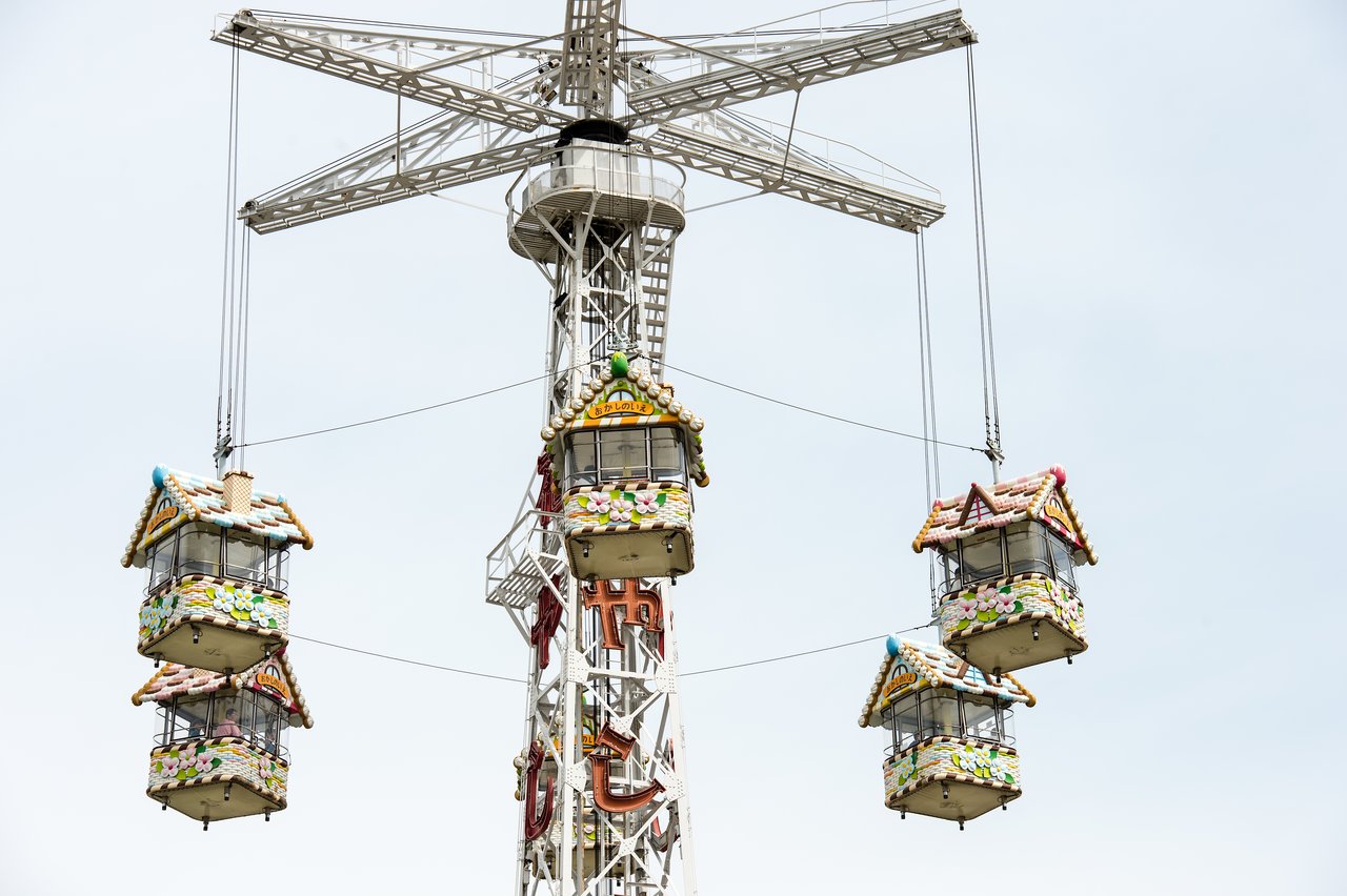 A tall amusement park ride with hanging gondolas shaped like colorful gingerbread houses, suspended by cables.