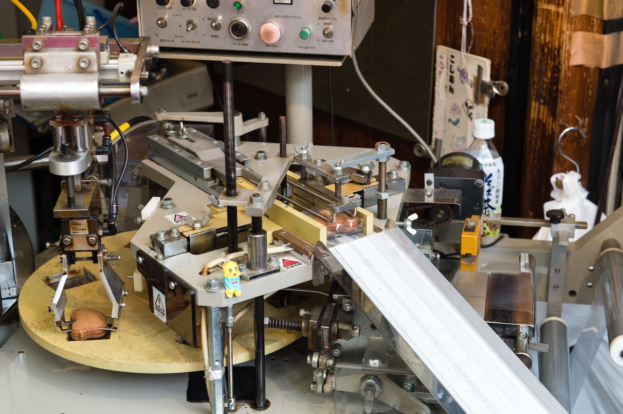 A packaging machine wraps small snacks in plastic film, with control buttons and levers visible on the device.