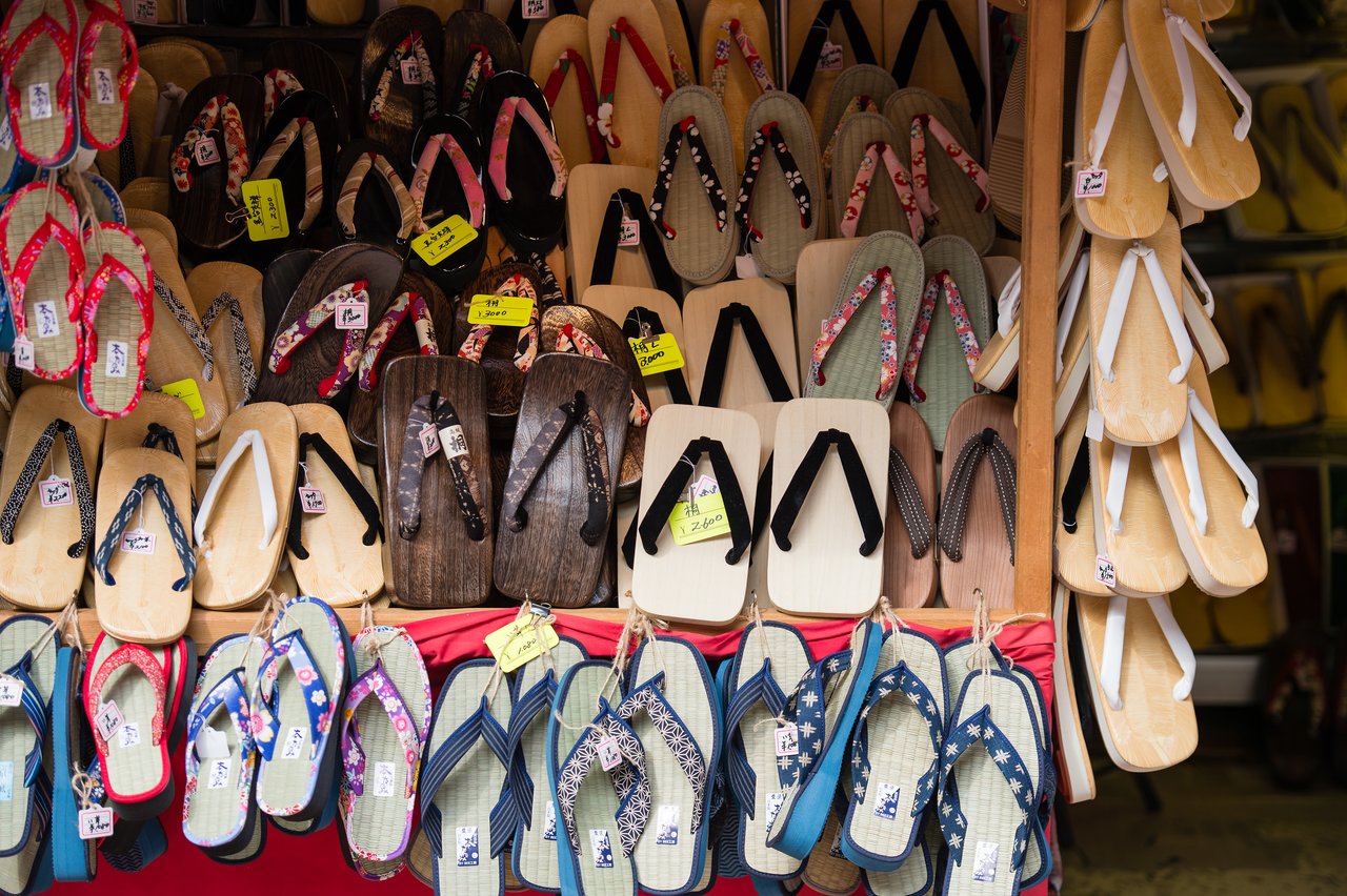 A market stall displays traditional Japanese wooden and straw sandals in various colors and patterns.