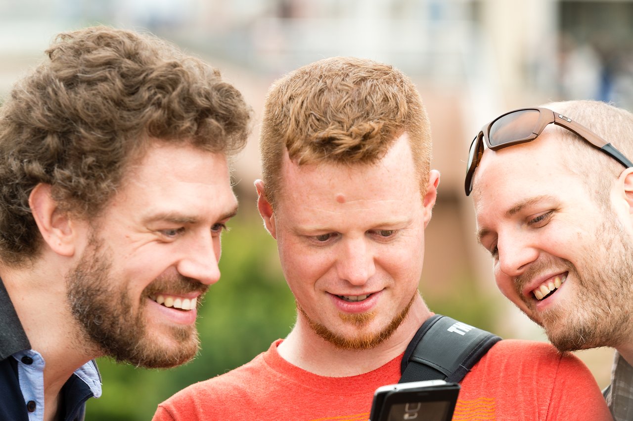 Three men smiling and looking at a smartphone screen together.